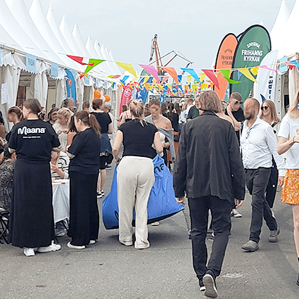 Med folkvimlet på Frihamnsdagarna 2024 och den blågrå himlen som bakgrund, förmedlar bilden en öppen och välkomnande atmosfär. Människor från olika bakgrunder samlas för att njuta av dagen, vilket skapar en känsla av gemenskap och tillhörighet.