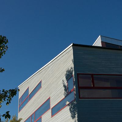 Grått hus som skuggas delvis av ett träd. Klarblå himmel.