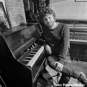 En man som avslappnat sitter invid ett piano.