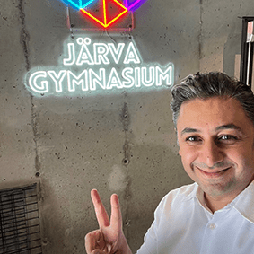 Glädje och stolthet när han gör ett segertecken med fingrarna. Neontext på väggen: Järva Gymnasium.